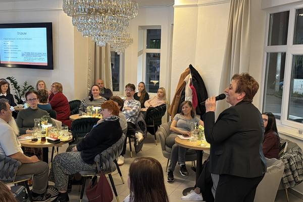 The host with a microphone in front of a packed café, with a slide about Dr Maxim’s studies on the screen